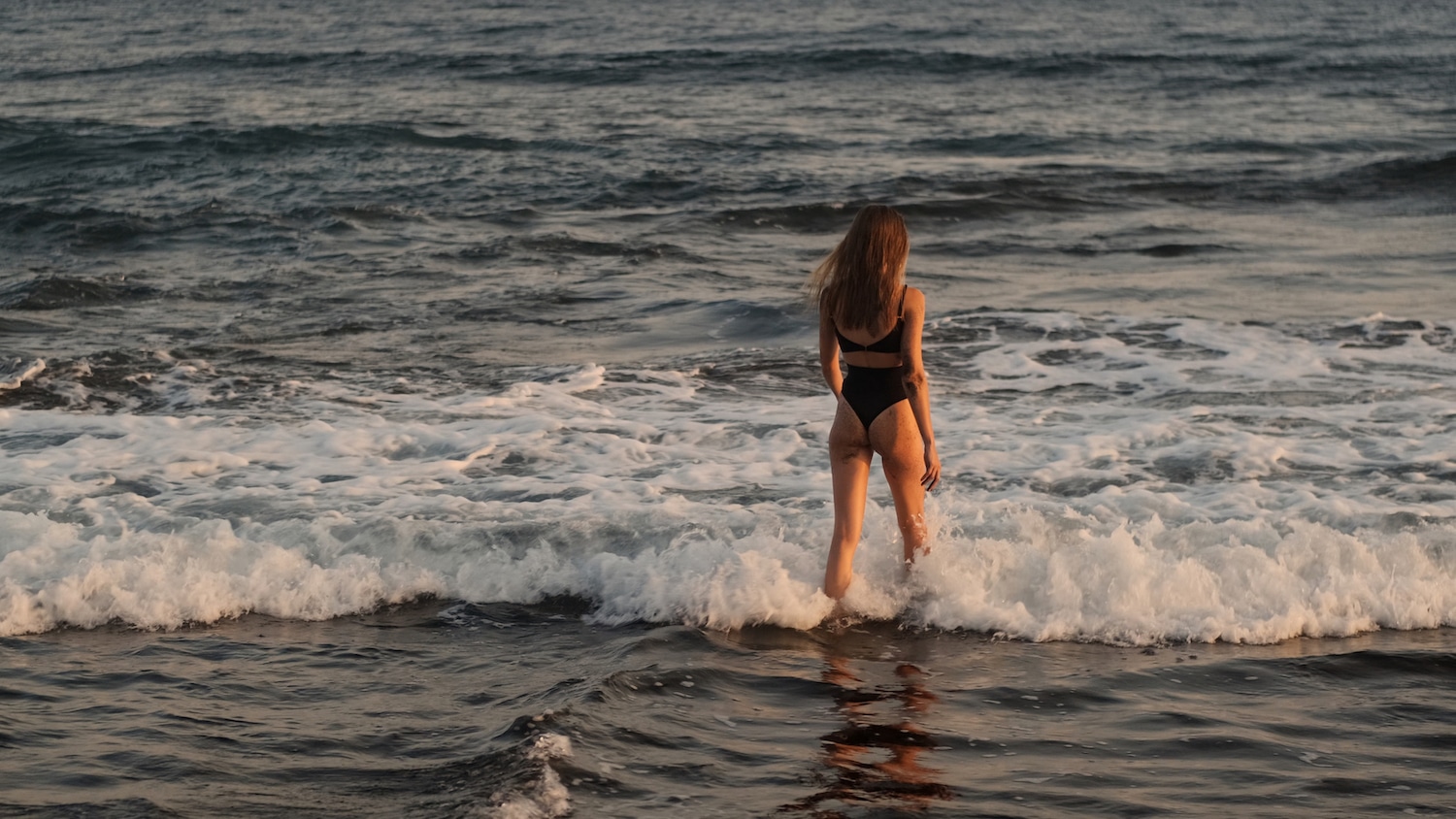 Back view of beautiful slim girl swimming in ocean resting on tropical island