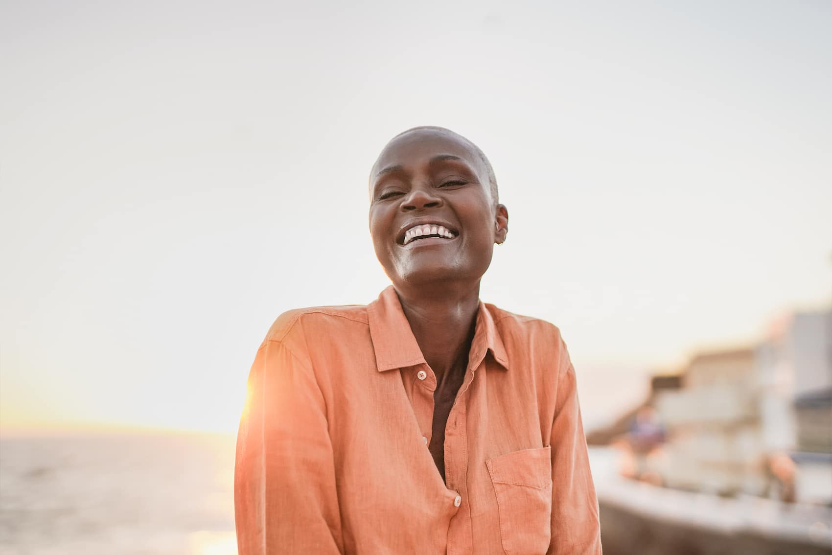 Mature African woman smiling on camera outdoor with ocean and sunset in background