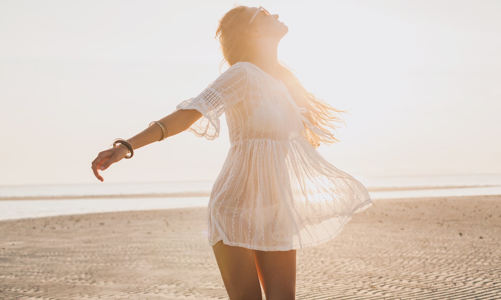 slim beautiful woman in white cotton dress walking on tropical beach
