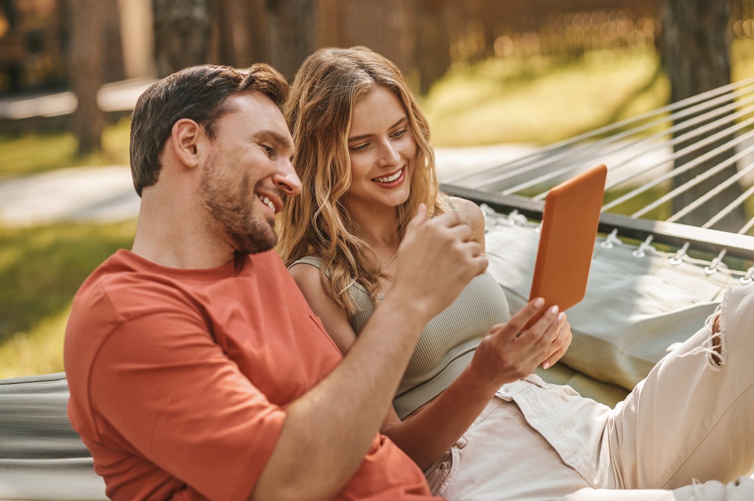 man and women happily looking at a tablet on a hammock