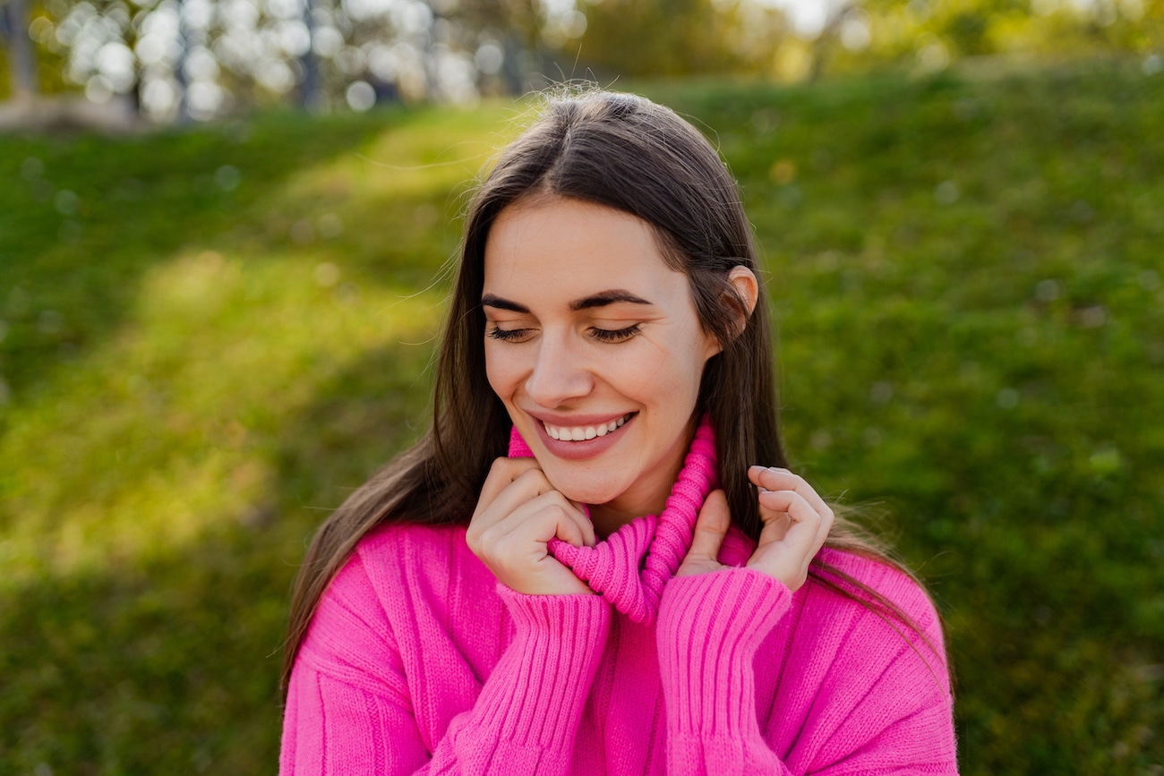 young smiling woman in pink sweater walking in green park