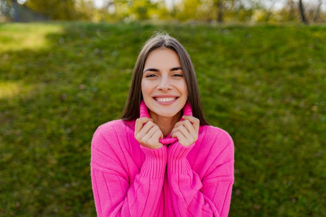 young smiling woman in pink sweater walking in green park