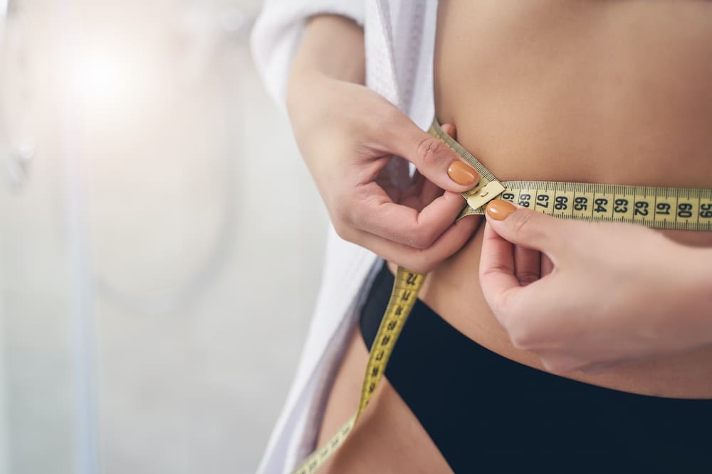 Close up of slim lady wrapping yellow measuring tape feeling slimmer after non-surgical fat removal in houston