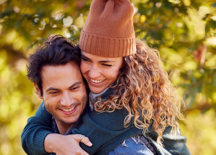Happy Loving Couple Smiling As Man Give Woman Piggyback In Autumn Park after treatment for peyronie's disease in houston