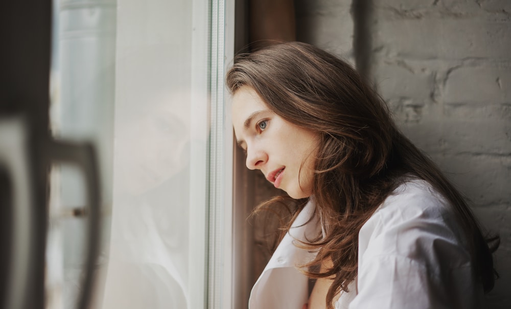 Young beautiful woman in white shirt laying her head in the glass window