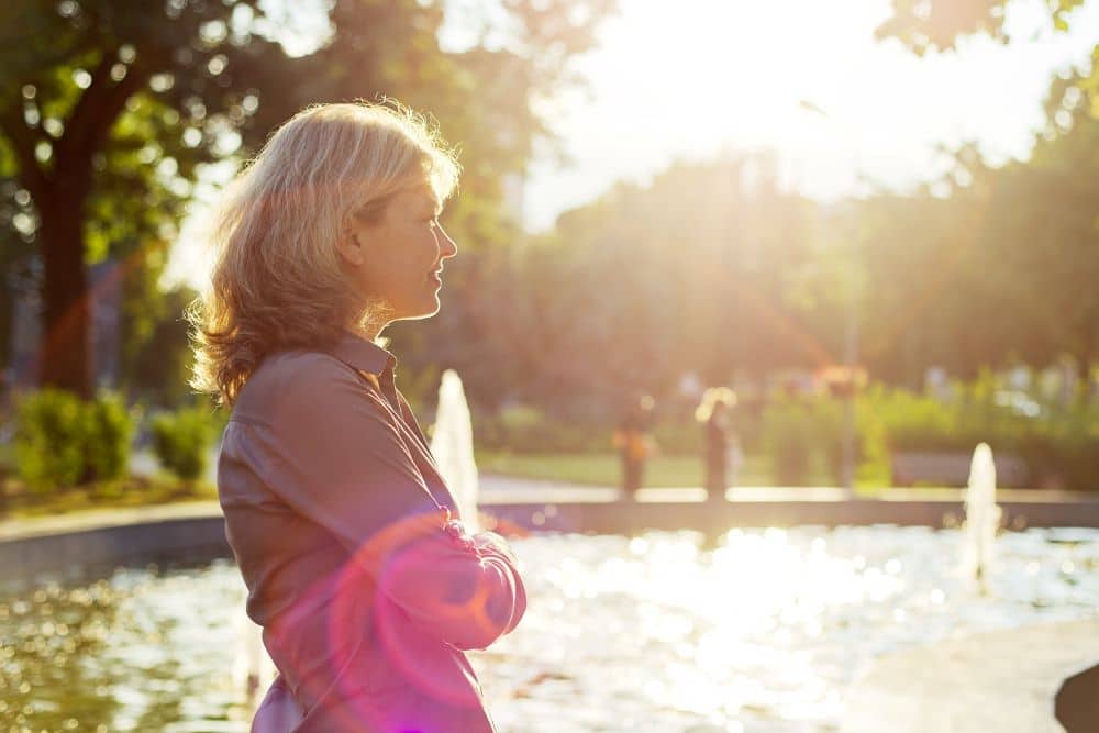 Woman standing beside the pond with water fountain looking far in the horizon