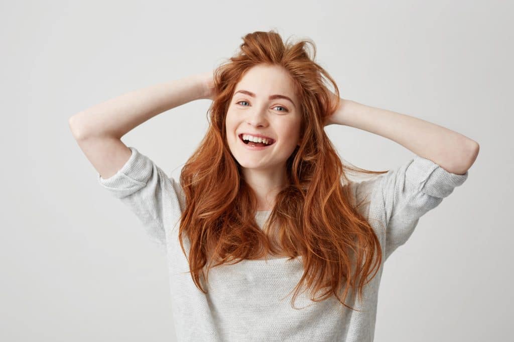Portrait of happy young beautiful redhead girl smiling looking at camera touching hair over white background. hair restoration houston