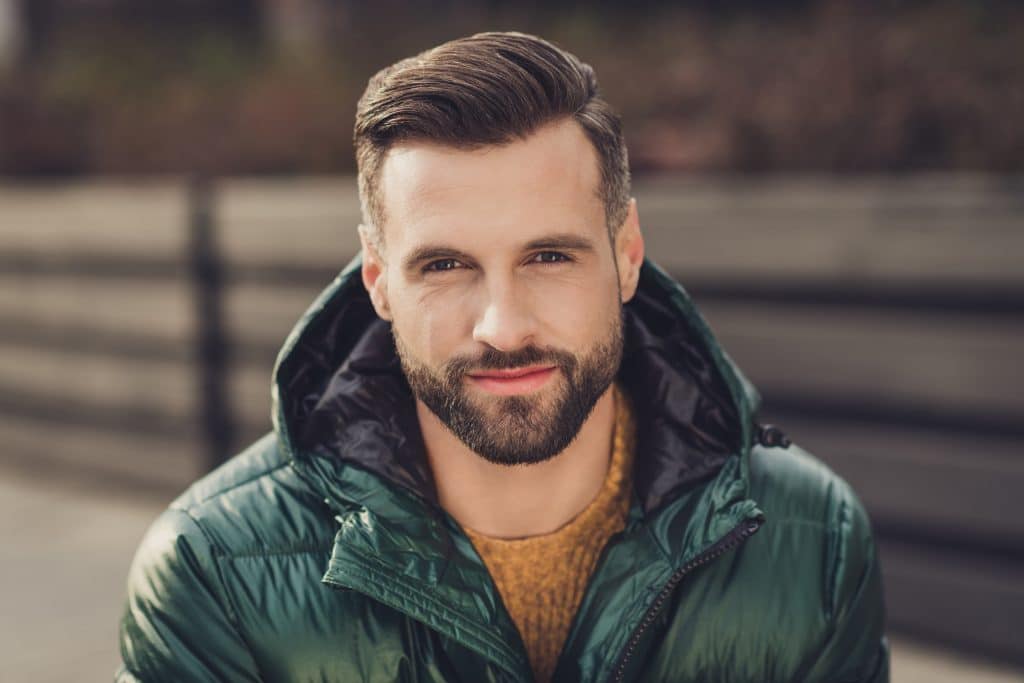 Photo of charming cute confident young guy dressed green coat smiling having rest outdoors city street hair loss restoration houston