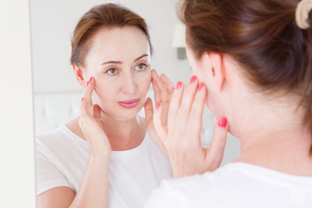 Middle age woman looking in mirror on face. Wrinkles and anti aging skin care concept. Selective focus bhrt houston